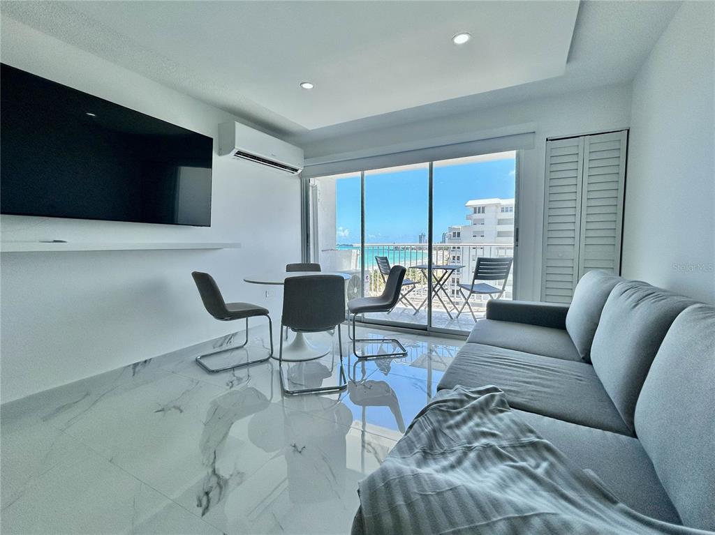 A modern living room features white marble floors, a grey sofa, and a balcony with ocean views — 4837 AVE ISLA VERDE UNIT 607, CAROLINA, PR