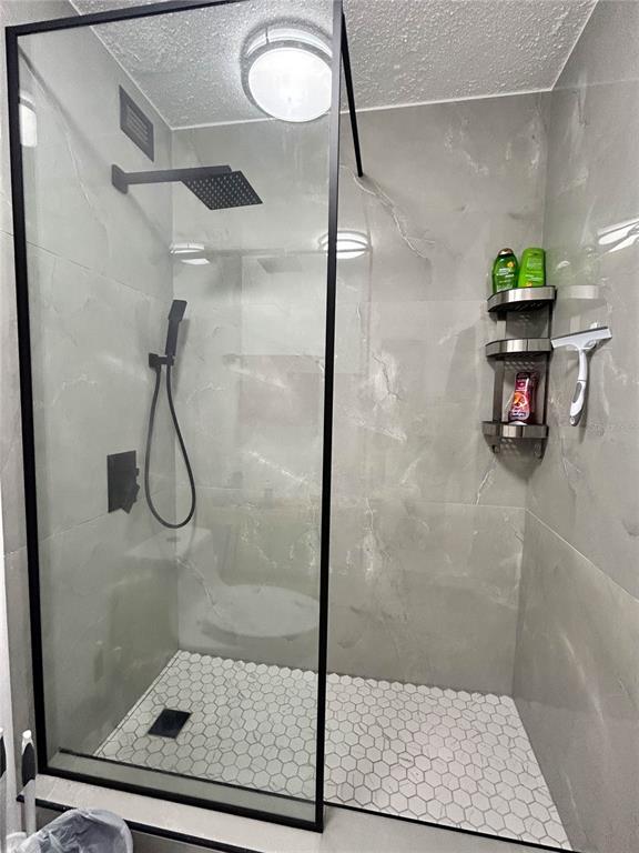 A walk-in shower features a black frame, rainfall showerhead, and gray marble-look tile walls — 4837 AVE ISLA VERDE UNIT 607, CAROLINA, PR