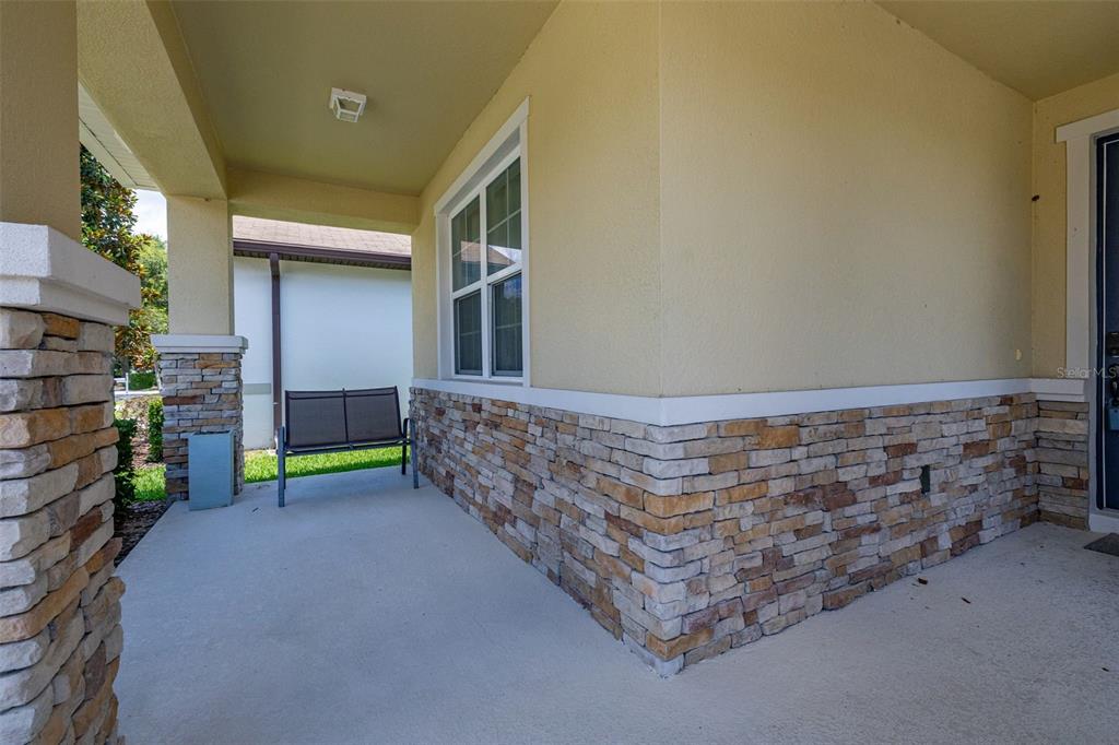A covered front porch features stone veneer siding, a concrete floor, and a metal bench — 1222 YORKSHIRE COURT, DAVENPORT, FL