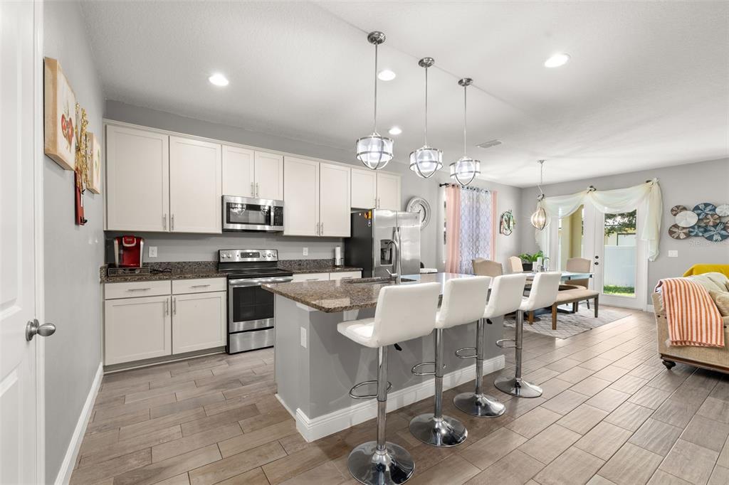 A modern kitchen features white cabinets, granite countertops, a center island, and stainless steel appliances — 1222 YORKSHIRE COURT, DAVENPORT, FL