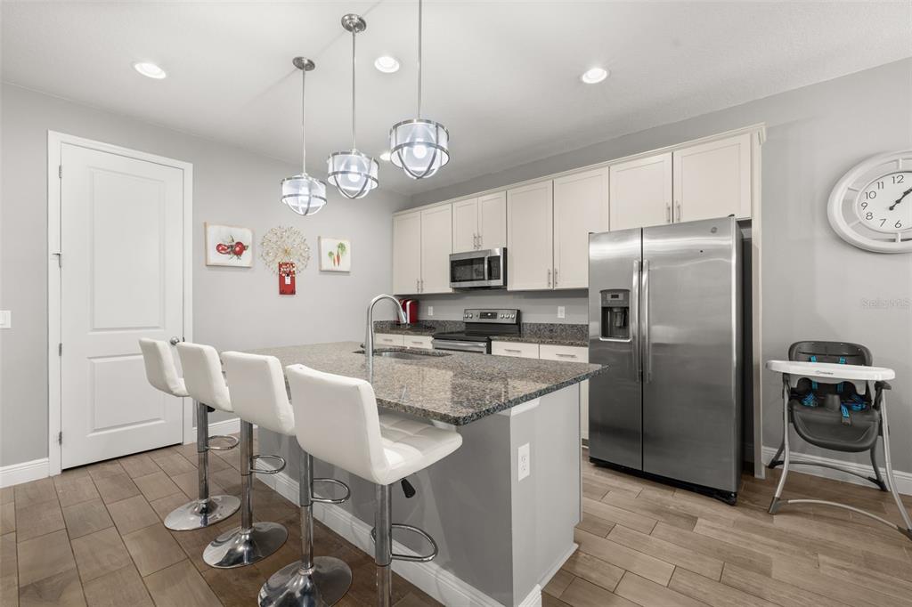 A kitchen features a granite-topped island with bar seating, stainless steel appliances, and white cabinetry — 1222 YORKSHIRE COURT, DAVENPORT, FL
