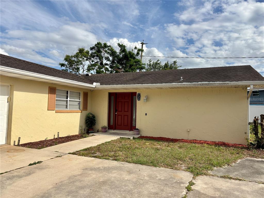 A single-story house with yellow stucco walls, a red front door, and a concrete driveway — 728 LAKE NED ROAD, WINTER HAVEN, FL