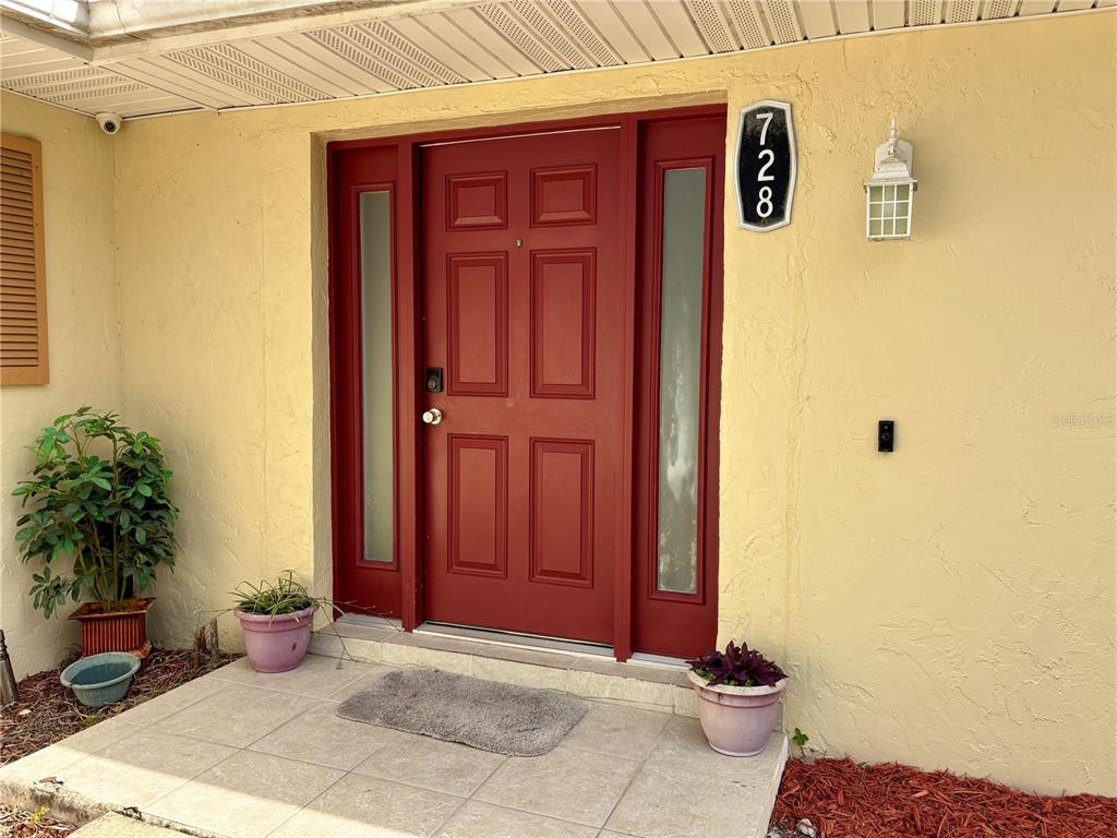 A red front door with sidelights is centered on a yellow stucco exterior wall — 728 LAKE NED ROAD, WINTER HAVEN, FL