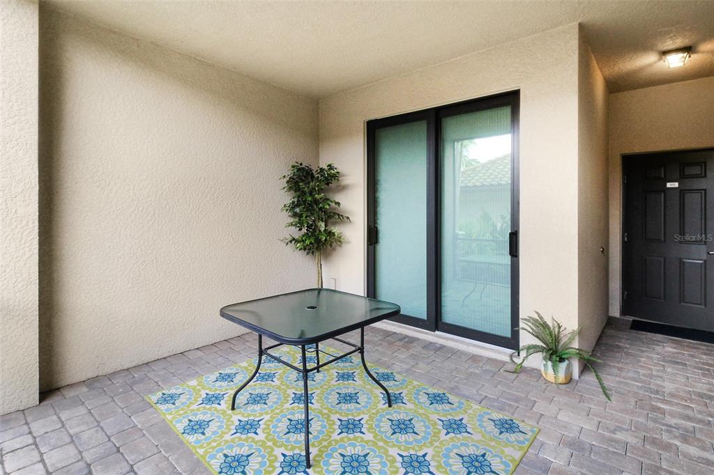 A covered patio features a glass-top table, a patterned rug, and a sliding glass door — 5517 PALMER CIRCLE UNIT 105, BRADENTON, FL