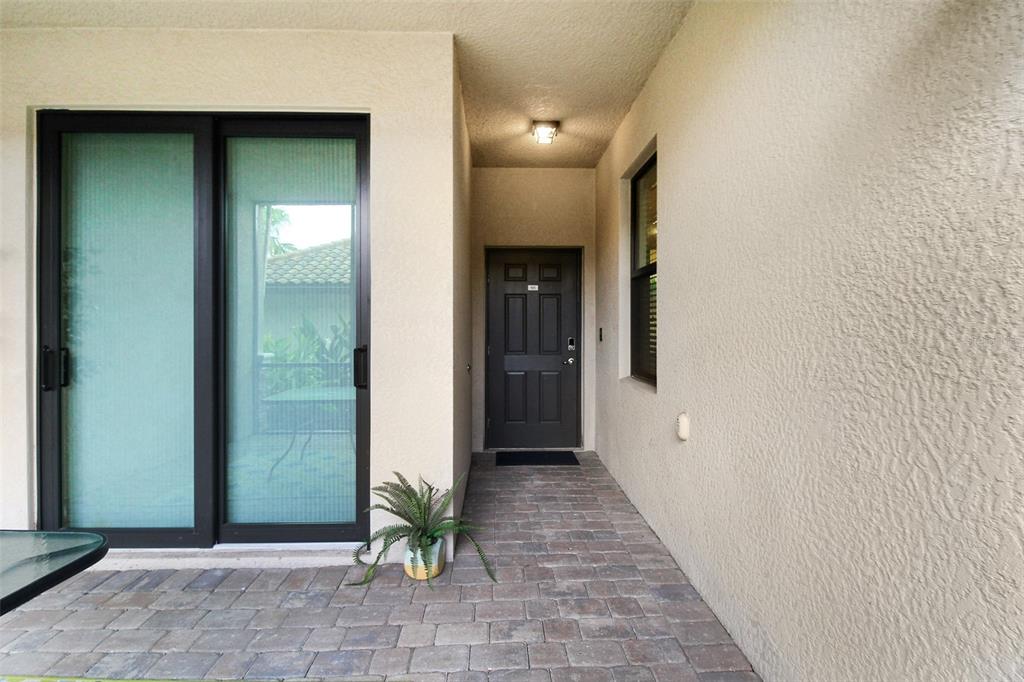 A covered patio features a dark door, a sliding glass door, and paver flooring — 5517 PALMER CIRCLE UNIT 105, BRADENTON, FL