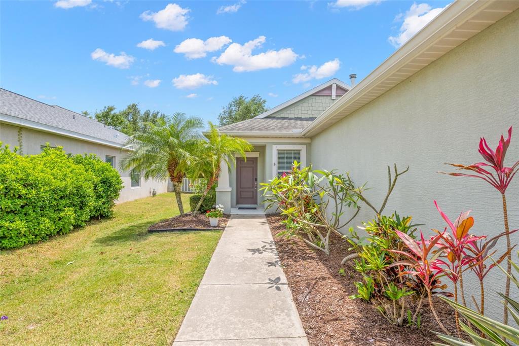A concrete walkway leads to the front entrance of a house with light-colored stucco siding — 4919 BOSTON COMMON GLEN, BRADENTON, FL