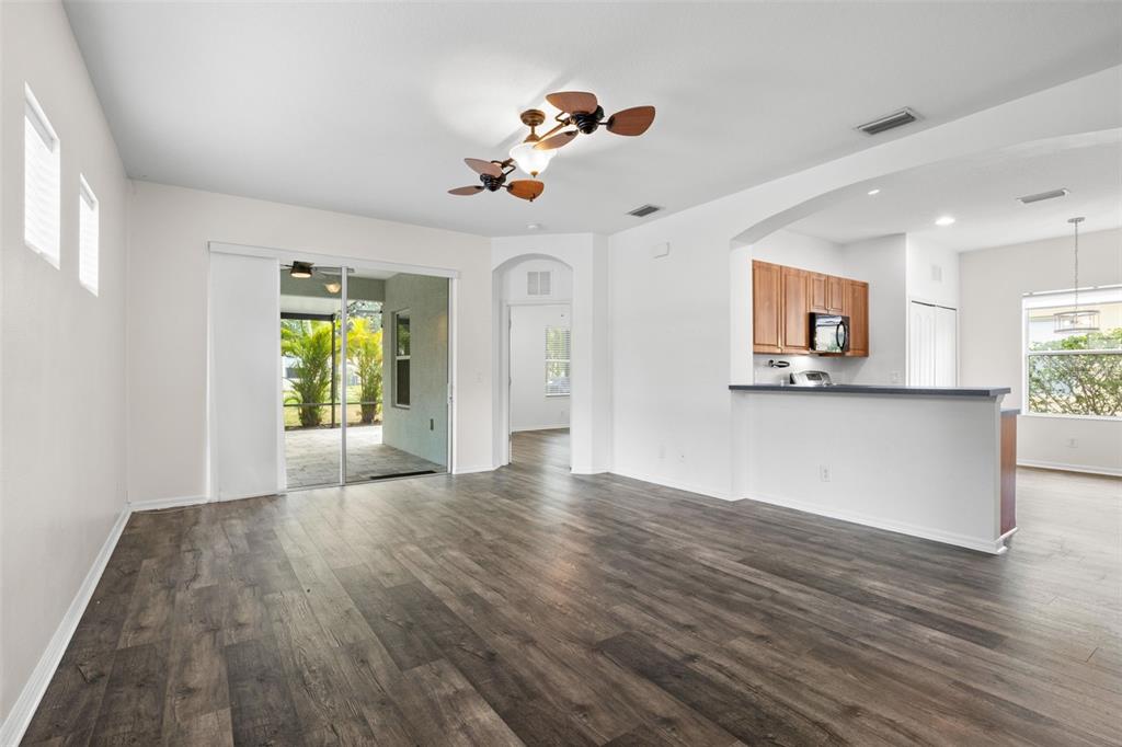 An open-concept living area features dark wood-look flooring, a ceiling fan, and a kitchen pass-through — 4919 BOSTON COMMON GLEN, BRADENTON, FL