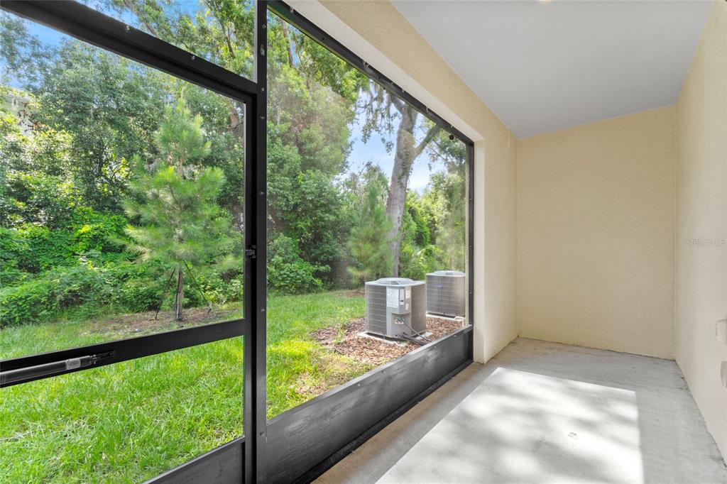 A screened-in porch with a concrete floor overlooks a grassy yard with two air conditioning units — 5137 BENJAMIN ERIC STREET, ZEPHYRHILLS, FL