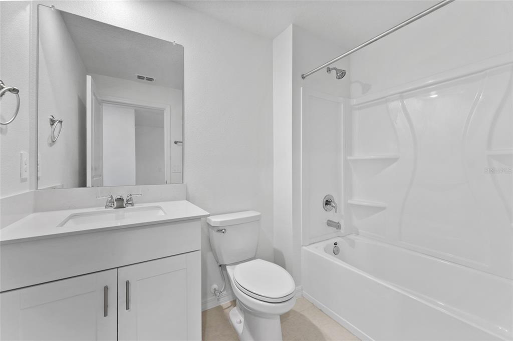 A white bathroom features a vanity with a sink, a toilet, and a shower-tub combo — 5137 BENJAMIN ERIC STREET, ZEPHYRHILLS, FL