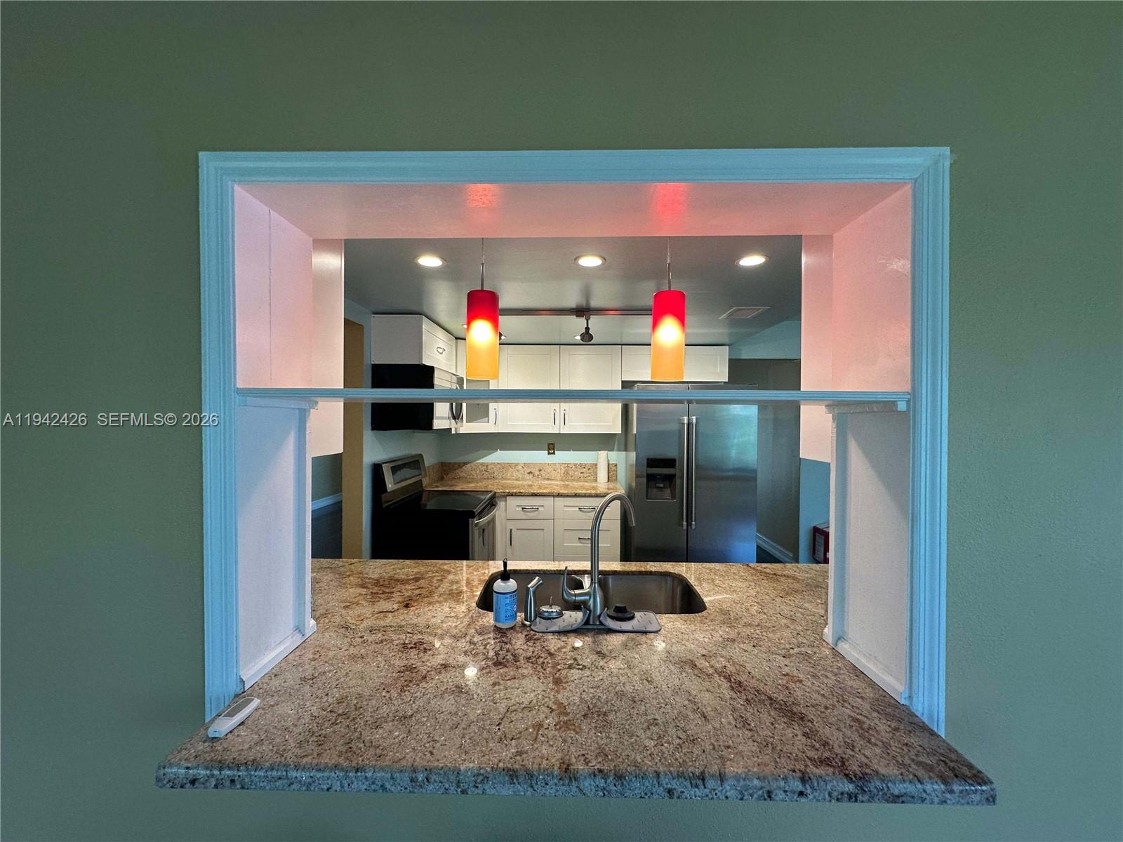 A kitchen pass-through window features a granite countertop, stainless steel sink, and pendant lighting — 4701 NW 44th St, Tamarac FL 33319, TAMARAC, FL
