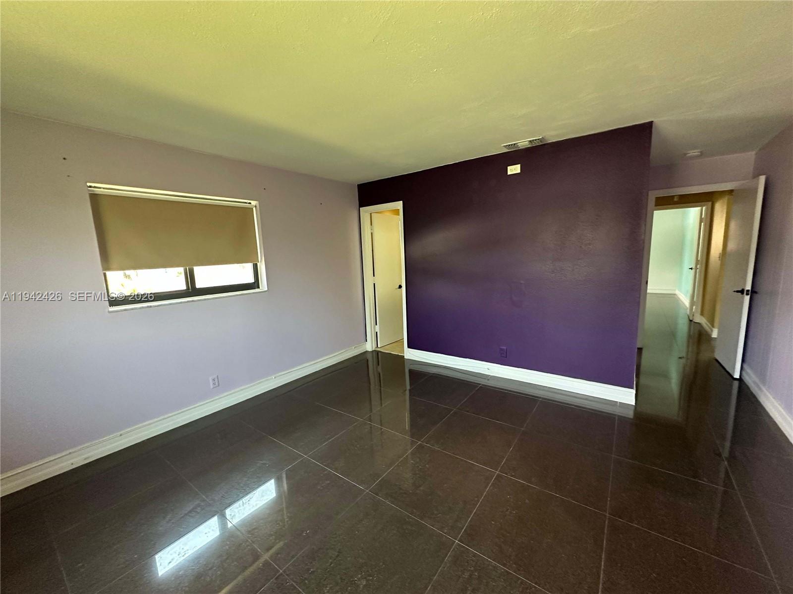 An empty room features dark tile flooring, a purple accent wall, and a window — 4701 NW 44th St, Tamarac FL 33319, TAMARAC, FL