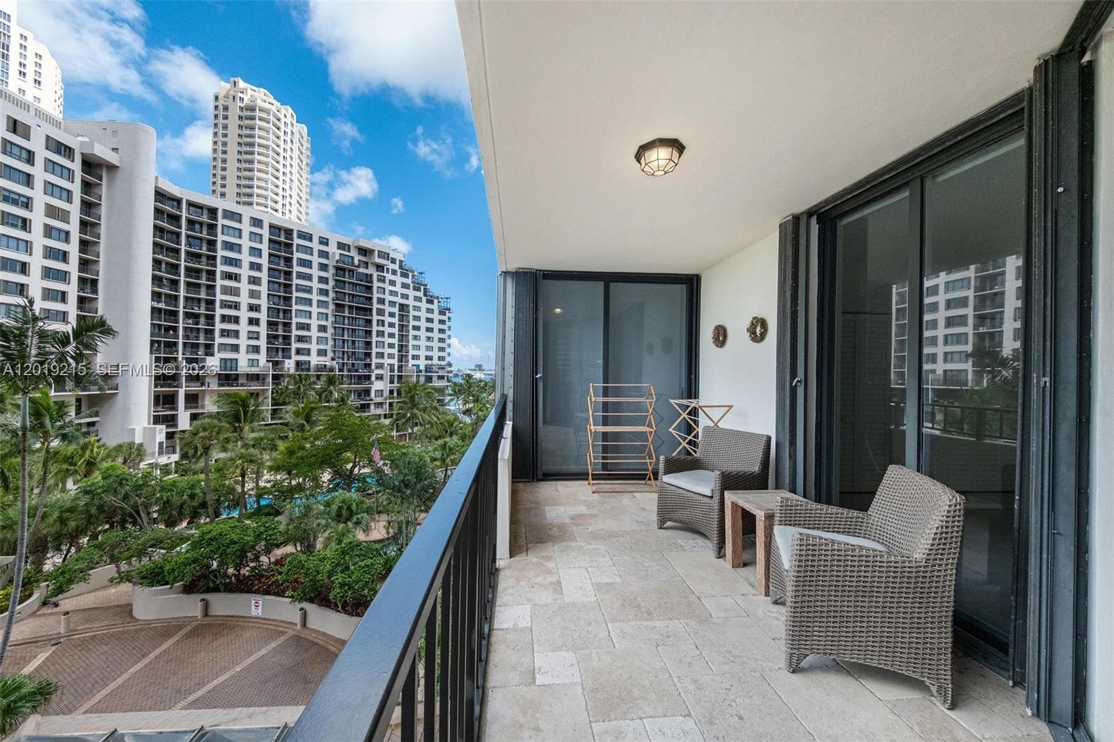 A balcony with stone flooring, two wicker chairs, and a view of surrounding apartment buildings — 520 Brickell Key Dr # A710, Miami FL 33131, MIAMI, FL