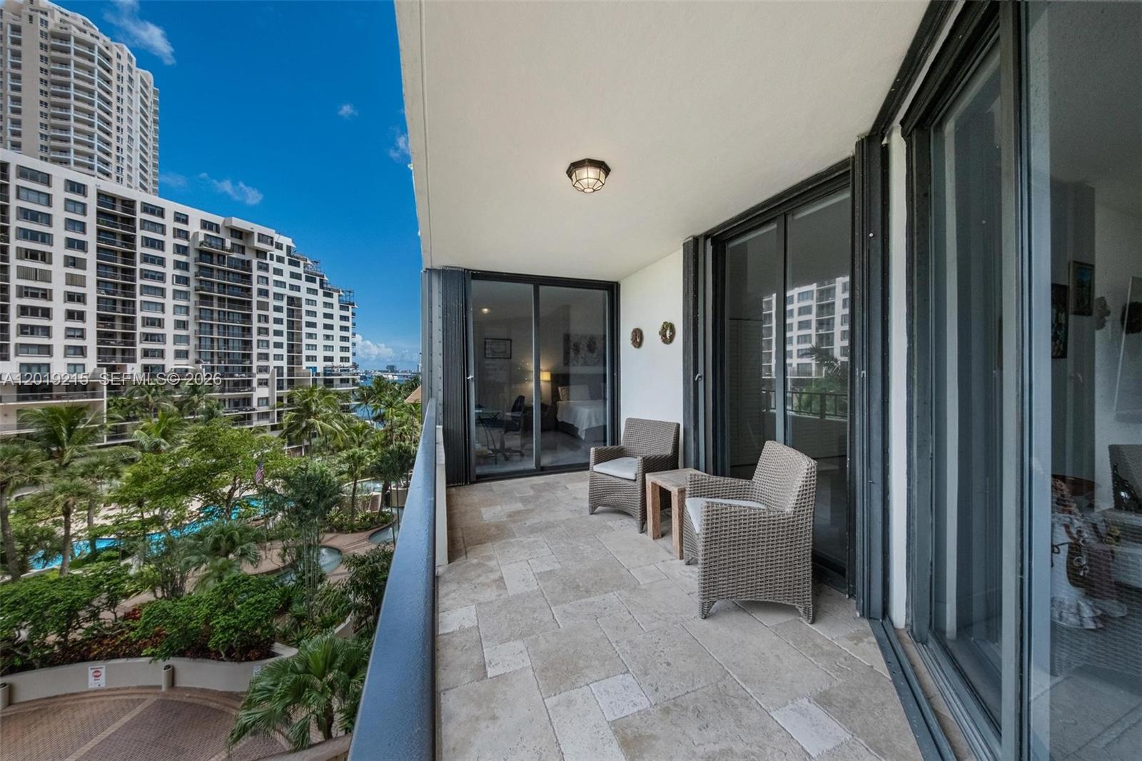 A balcony with stone flooring, two wicker chairs, and a view of surrounding apartment buildings — 520 Brickell Key Dr # A710, Miami FL 33131, MIAMI, FL