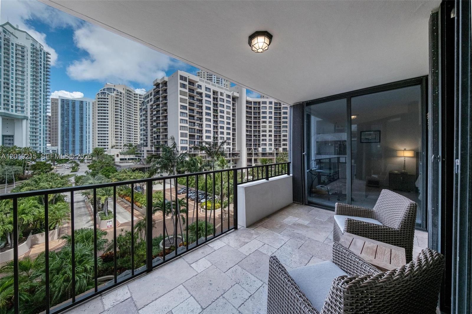 A balcony with stone flooring, wicker chairs, and a metal railing overlooks urban high-rise buildings — 520 Brickell Key Dr # A710, Miami FL 33131, MIAMI, FL