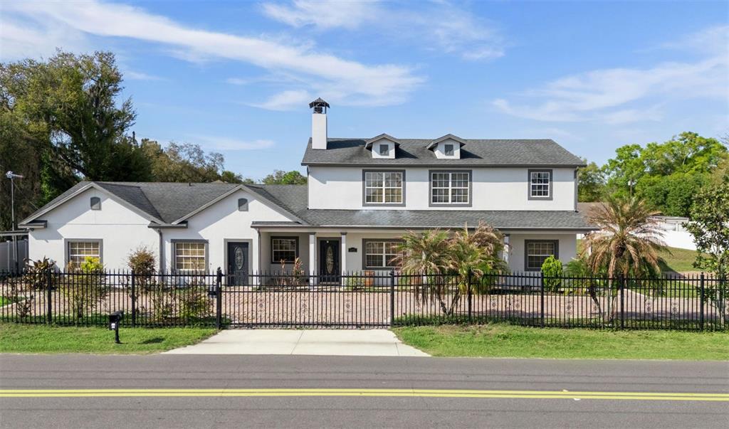 A two-story white house with a gray roof and a black metal fence in front — 6053 NEW HOPE ROAD, ORLANDO, FL