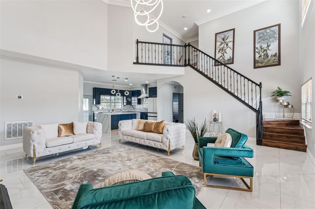 A high-ceilinged living room features white tufted sofas, teal armchairs, and a staircase with railing — 6053 NEW HOPE ROAD, ORLANDO, FL