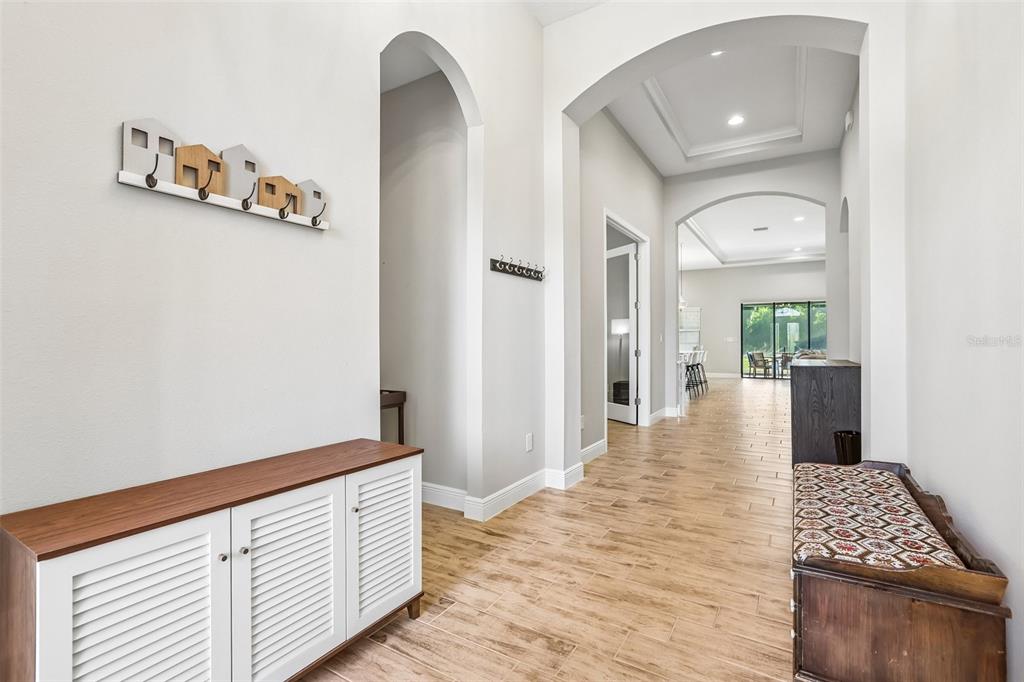 A bright entryway features wood-look tile flooring, arched doorways, a white cabinet, and a bench — 14142 SWISS BRIDGE DRIVE, RIVERVIEW, FL