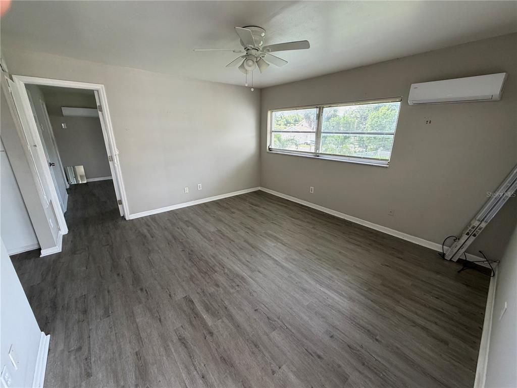An empty bedroom features gray wood-look flooring, a ceiling fan, and a wall-mounted air conditioner — 615 OAK AVENUE, CLEARWATER, FL