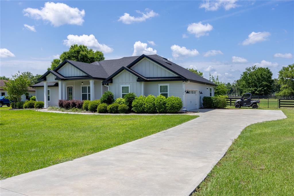 A light-colored single-story house with a dark roof, concrete driveway, and manicured landscaping — 1146 SW MANDIBA DRIVE, LAKE CITY, FL