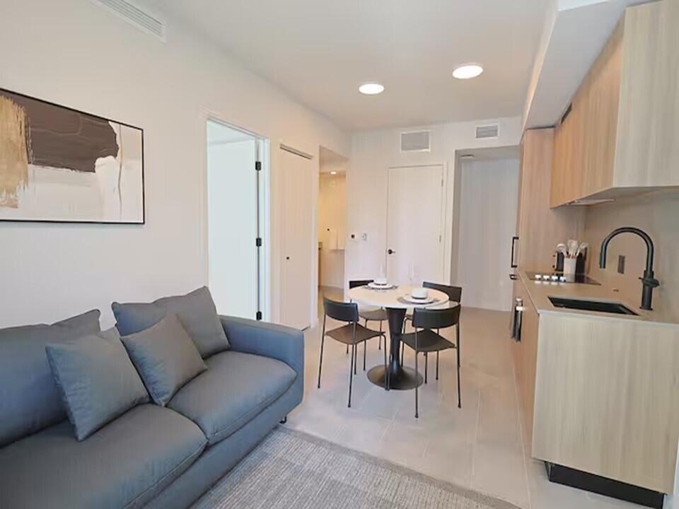 A small apartment living area with a grey sofa, dining table, and kitchenette — 121 NE 5th Street, Miami FL 33132, MIAMI, FL
