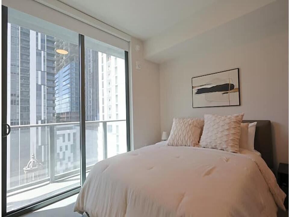 A bedroom with a white bed, abstract wall art, and a balcony overlooking city buildings — 121 NE 5th Street, Miami FL 33132, MIAMI, FL