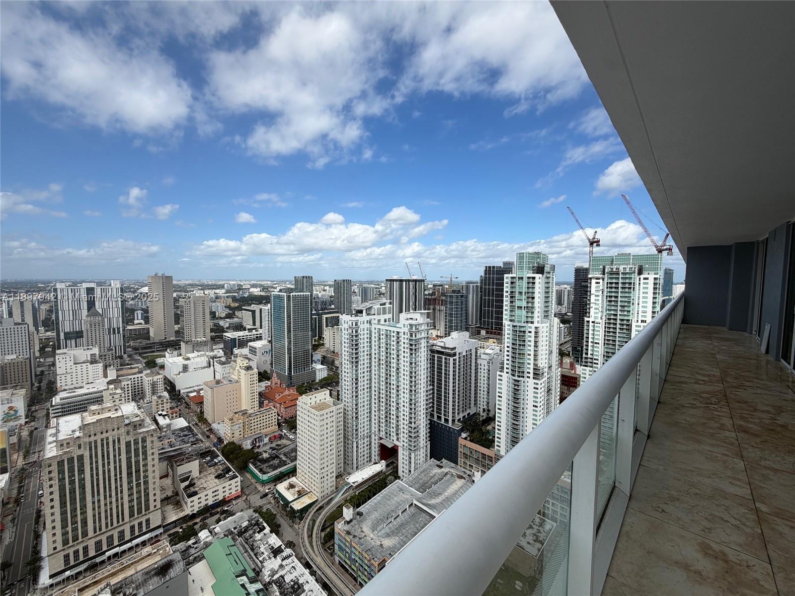 A high-rise balcony overlooks a dense urban cityscape with numerous skyscrapers and construction cranes — 50 Biscayne Blvd # 5211, Miami FL 33132, MIAMI, FL