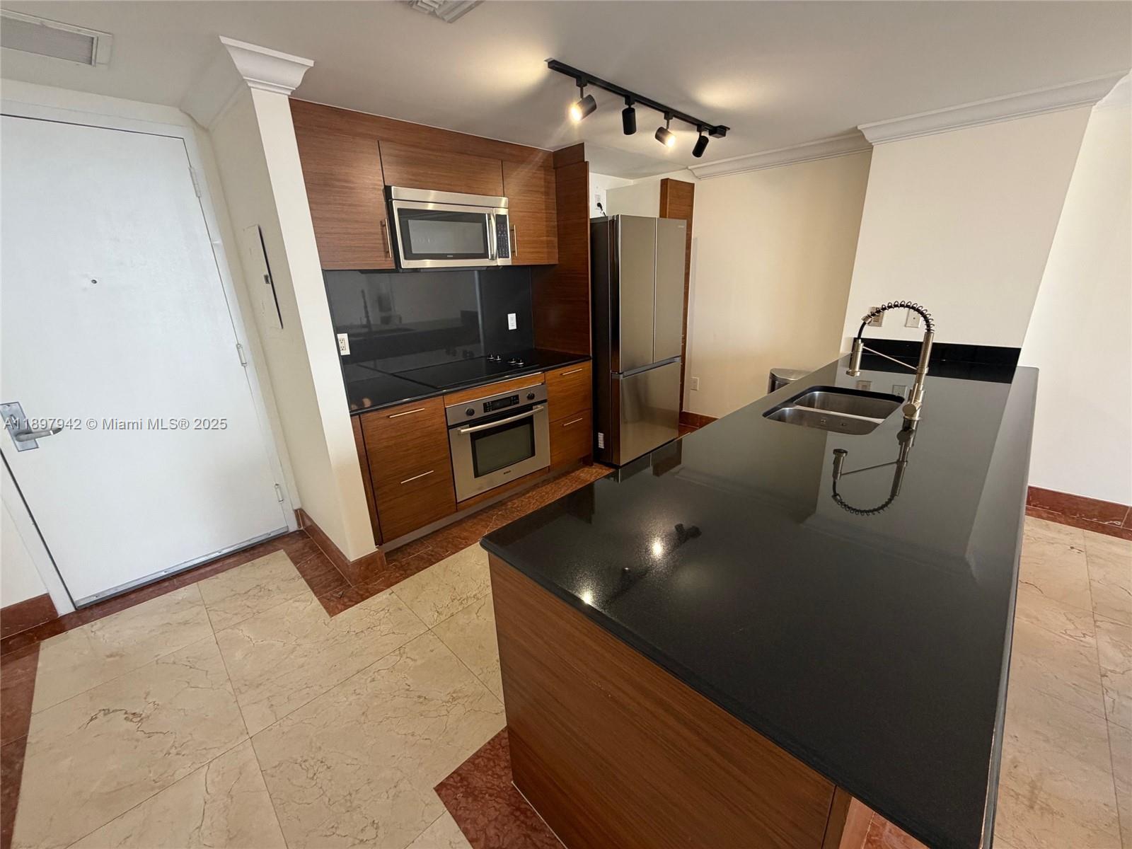 A kitchen features wood-grain cabinetry, black countertops, stainless steel appliances, and a large island — 50 Biscayne Blvd # 5211, Miami FL 33132, MIAMI, FL
