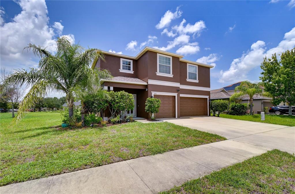 A two-story brown stucco house stands in a grassy yard under a cloudy sky — 2451 DAKOTA ROCK DRIVE, RUSKIN, FL