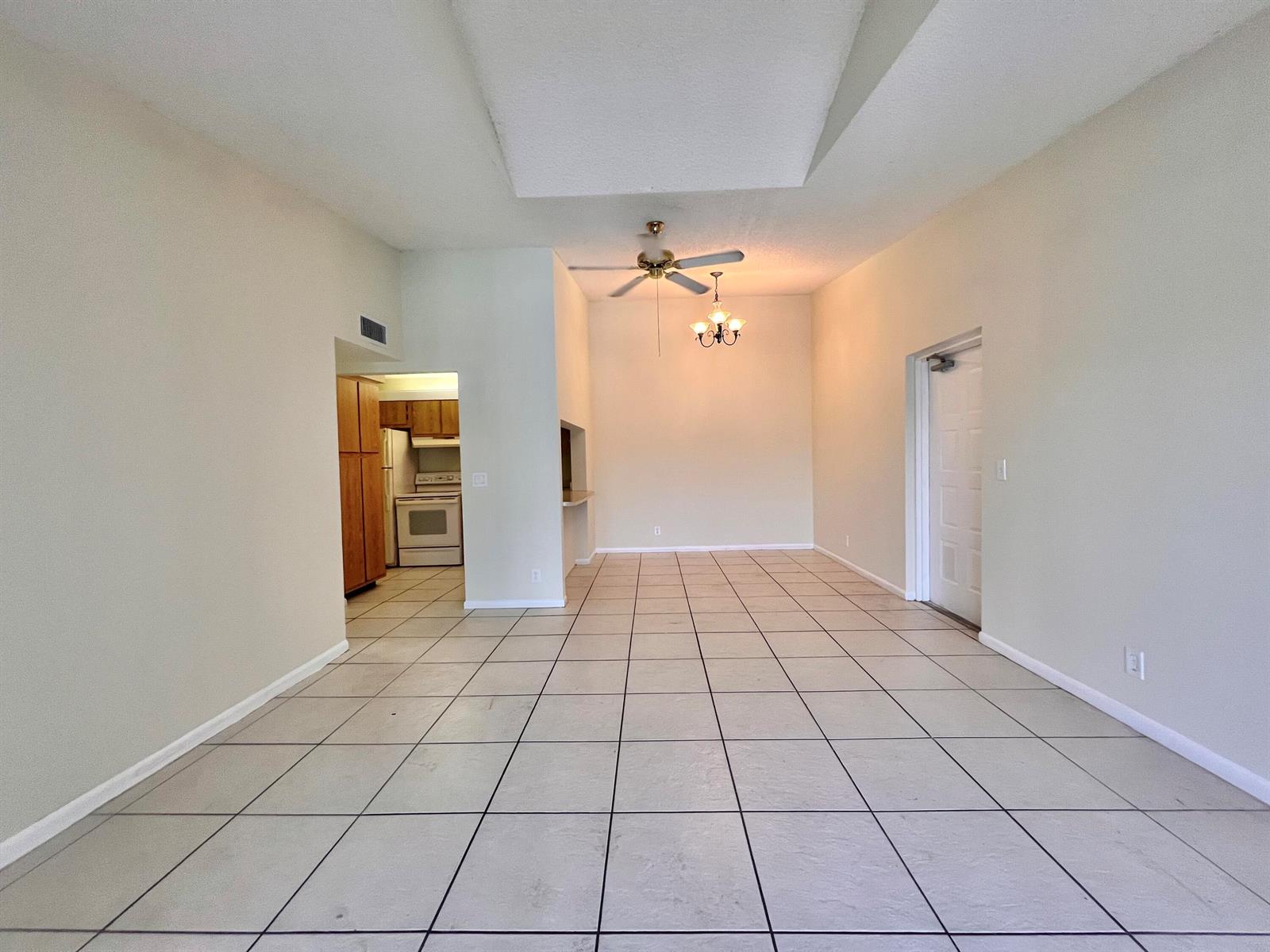 An empty room with light-colored tile flooring, a ceiling fan, and an adjacent kitchen — 1111 Green Pine Boulevard # C3, West Palm Beach FL 33409, WEST PALM BEACH, FL