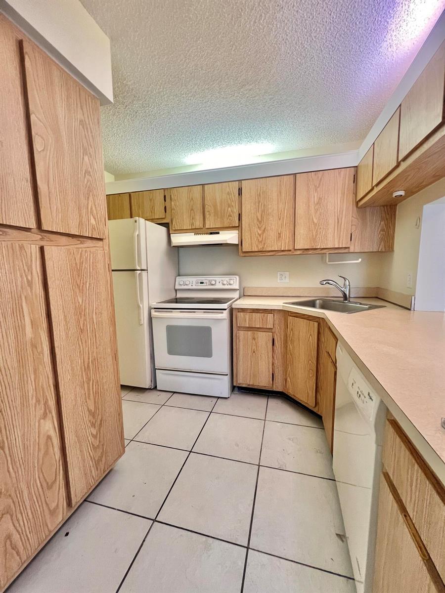 A kitchen features light wood cabinets, white appliances, a corner sink, and white tile flooring — 1111 Green Pine Boulevard # C3, West Palm Beach FL 33409, WEST PALM BEACH, FL