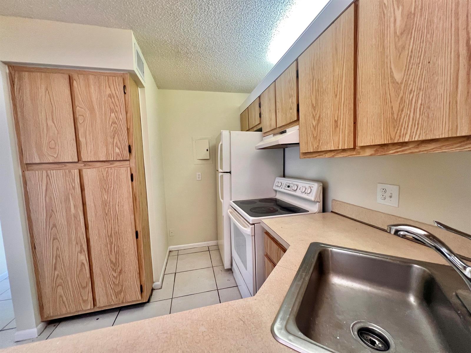 A kitchen features light wood cabinets, white appliances, a stainless steel sink, and tiled flooring — 1111 Green Pine Boulevard # C3, West Palm Beach FL 33409, WEST PALM BEACH, FL