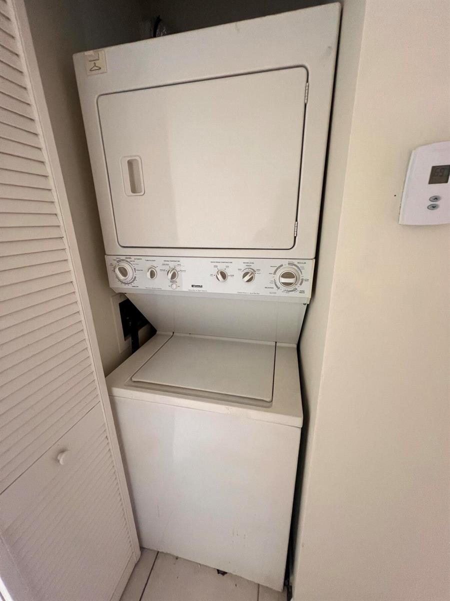 A white stacked washer and dryer unit is installed in a small laundry closet — 1111 Green Pine Boulevard # C3, West Palm Beach FL 33409, WEST PALM BEACH, FL