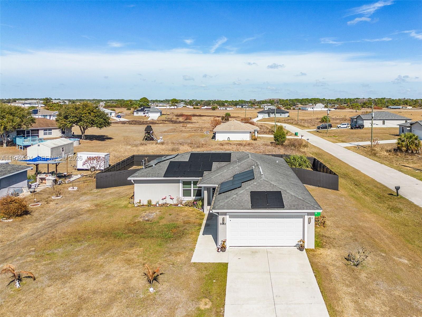 A backyard features a grassy lawn, a gravel patio area, and a wooden swing set — 9032 Meadow Circle, La Belle FL 33935, LA BELLE, FL