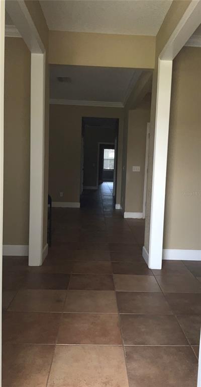 A hallway with tan walls and large square brown floor tiles leads to another room — 3613 S SUMMERLIN AVENUE, ORLANDO, FL