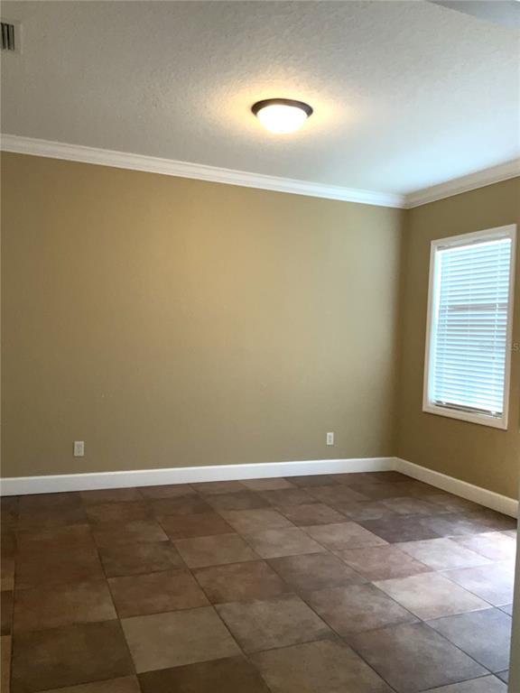An empty room features tan walls, a white ceiling with a light fixture, and tiled flooring — 3613 S SUMMERLIN AVENUE, ORLANDO, FL