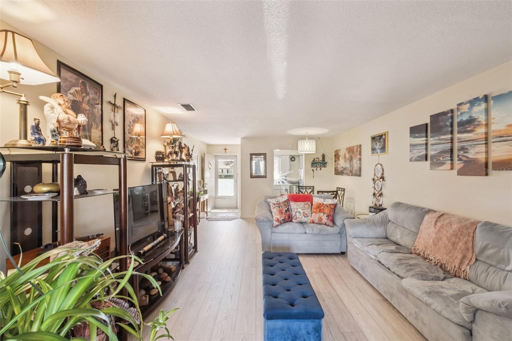 A living room features light wood-look flooring, a gray sofa, and a blue tufted ottoman — 714 E MINNESOTA AVENUE UNIT B, DELAND, FL