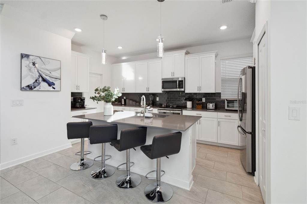 A modern kitchen features white cabinets, a gray island with bar stools, and tile flooring — 1009 LEADER, DAVENPORT, FL