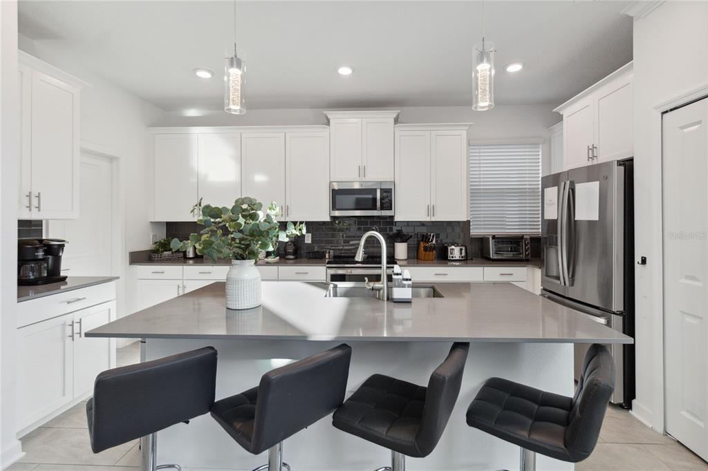 A modern kitchen features white cabinets, a large gray island with bar seating, and stainless appliances — 1009 LEADER, DAVENPORT, FL