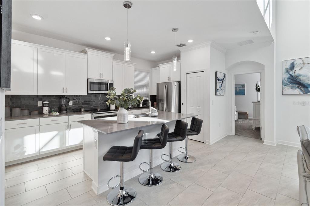A modern kitchen features white cabinets, a gray island with bar stools, and tile flooring — 1009 LEADER, DAVENPORT, FL