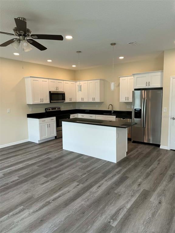 A kitchen features white cabinets, black countertops, a central island, and wood-look flooring — 4344 CAMBIO GARDENS COURT, TAMPA, FL