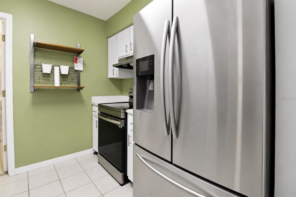 A kitchen with white cabinets, a stainless steel dishwasher, a corner sink, and green walls — 2523 NW 38 PLACE, GAINESVILLE, FL