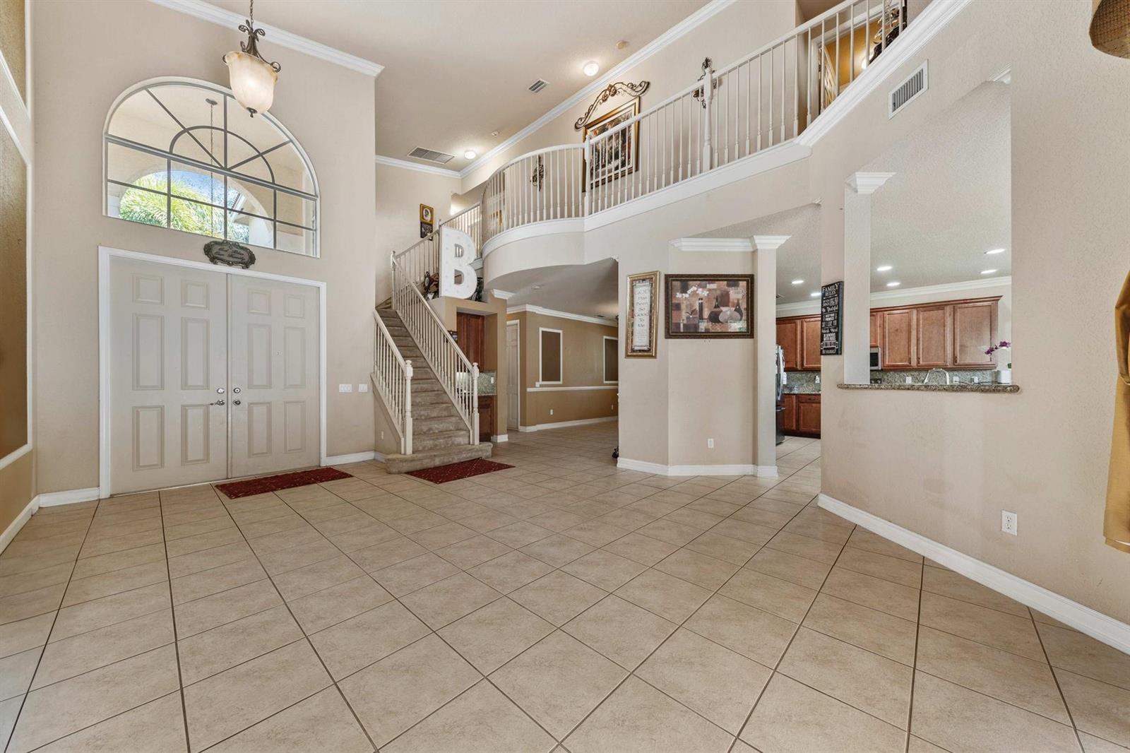 A spacious foyer features tile flooring, a grand staircase, and a view into the kitchen — 11729 Rock Lake Terrace, Boynton Beach FL 33473, BOYNTON BEACH, FL