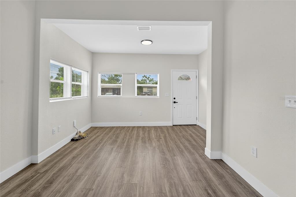 An empty room with light gray walls, wood-look flooring, multiple windows, and a white door — 2525 W BEACH STREET, TAMPA, FL