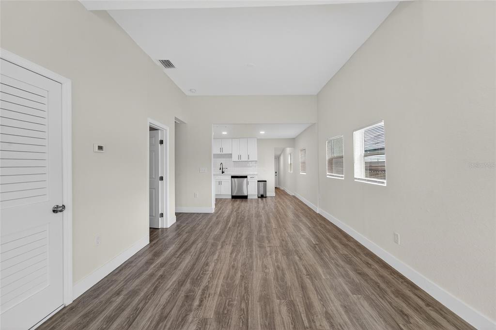 A bright, open-concept room features wood-look flooring, white walls, and a distant kitchen area — 2525 W BEACH STREET, TAMPA, FL