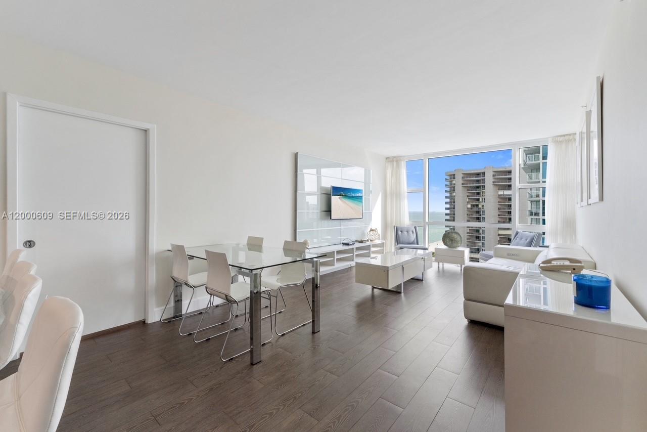 A modern living and dining area features white furniture, dark wood floors, and floor-to-ceiling windows — 6801 Collins Ave, Miami Beach FL 33141, MIAMI BEACH, FL