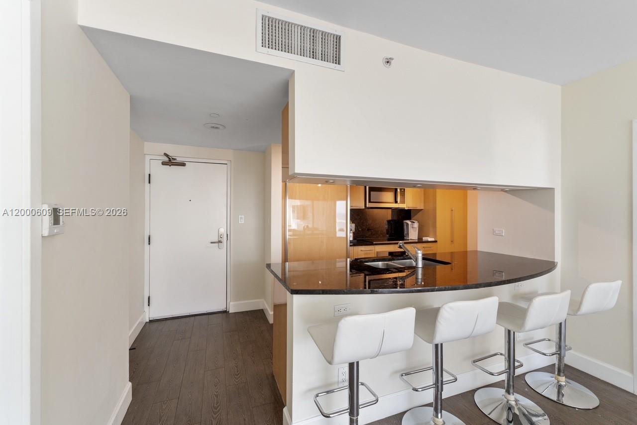 A kitchen with a dark granite breakfast bar and white stools overlooks a hallway — 6801 Collins Ave, Miami Beach FL 33141, MIAMI BEACH, FL