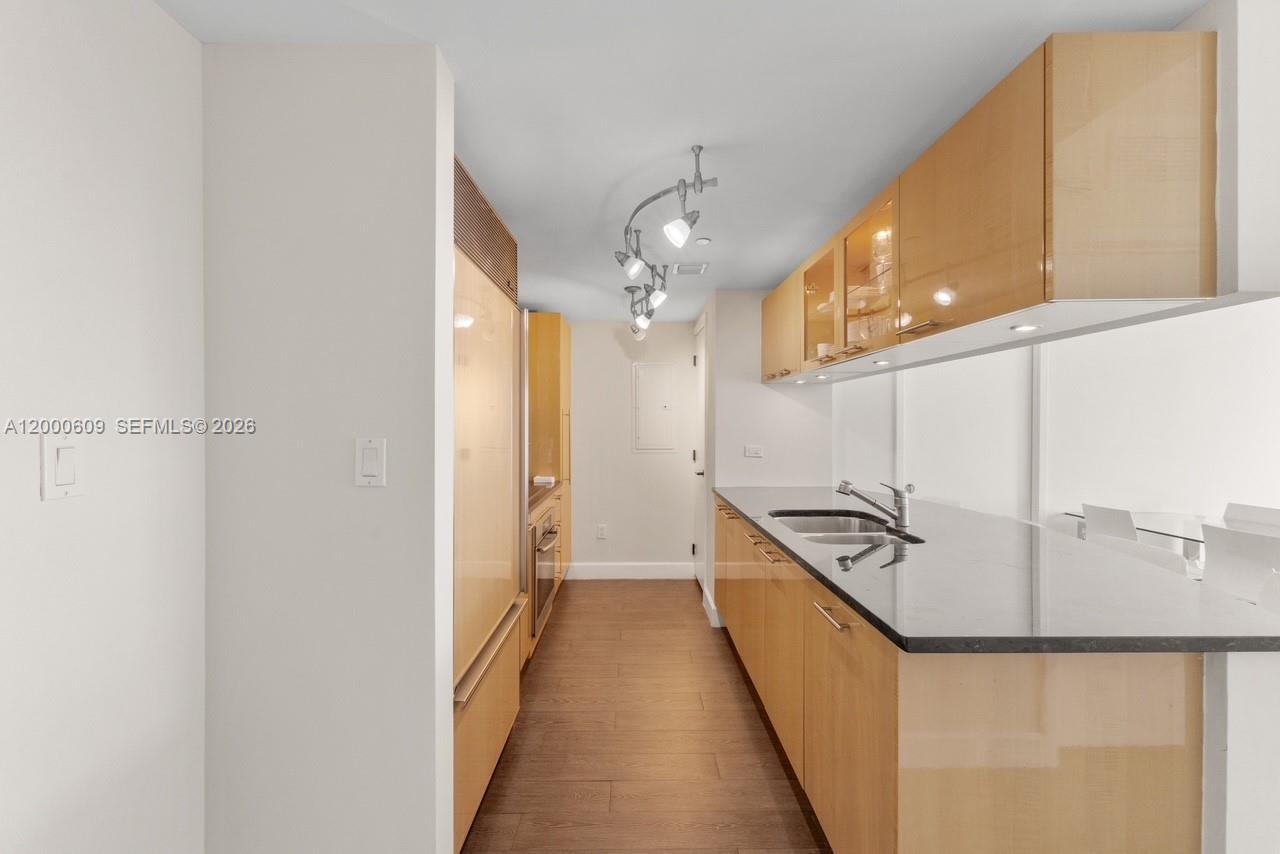 A galley kitchen features light wood cabinets, black countertops, and wood-look flooring — 6801 Collins Ave, Miami Beach FL 33141, MIAMI BEACH, FL