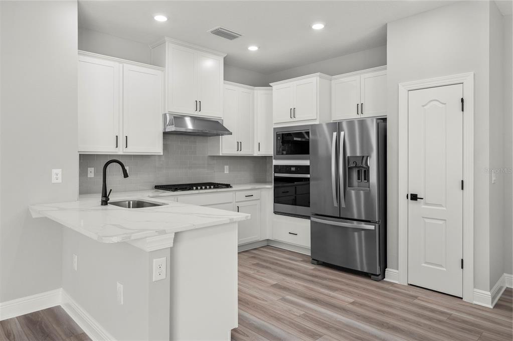 A modern kitchen features white cabinetry, stainless steel appliances, a marble-look island, and wood-look flooring — 7879 SOMERSWORTH DRIVE, KISSIMMEE, FL