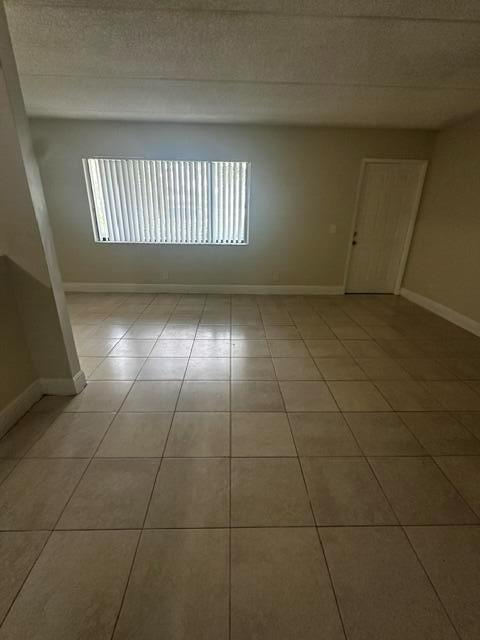 An empty room features light-colored floor tiles, a large window with vertical blinds, and a door — 704 Meadows Circle # 704, Boynton Beach FL 33436, BOYNTON BEACH, FL
