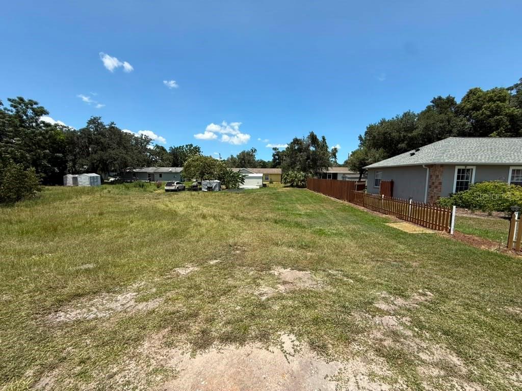 A grassy, vacant residential lot sits next to a house with a wooden fence — 27283 THRUSH AVENUE, BROOKSVILLE, FL